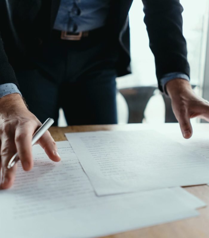 Close up hands signing documents in a modern office with window in background. Pen in hand, papers on the wooden desk, futuristic background.